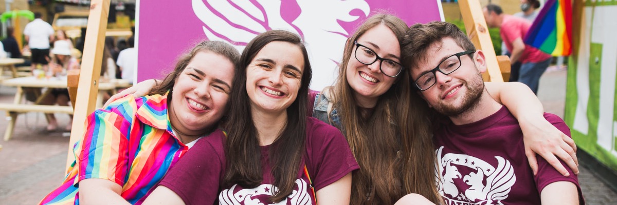 4 students sit in a large deckchair outside one of Lancaster's colleges