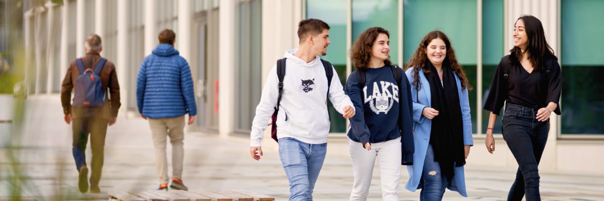 Four students walking past a modern building and flowerbeds.