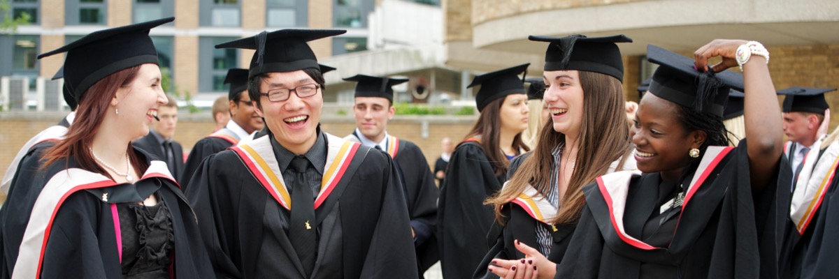 Four students in graduation gowns share a joke.