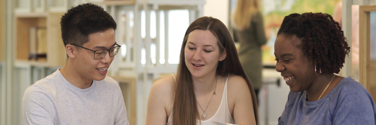 Three students laugh whilst working around a table