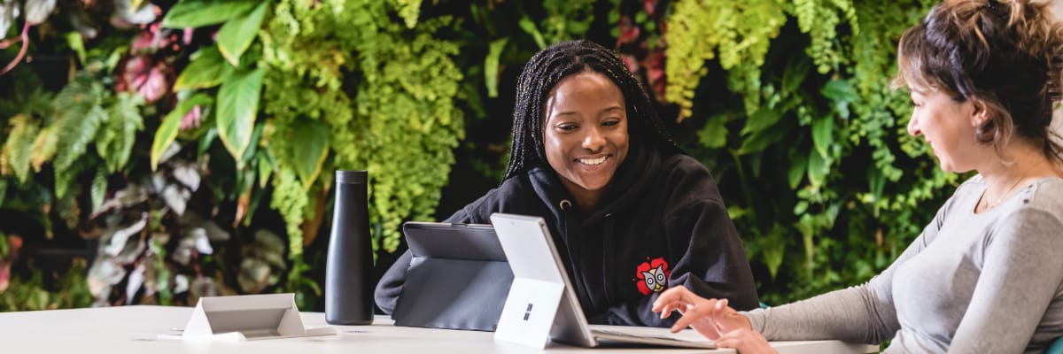 Two students in the Library by the green wall.
