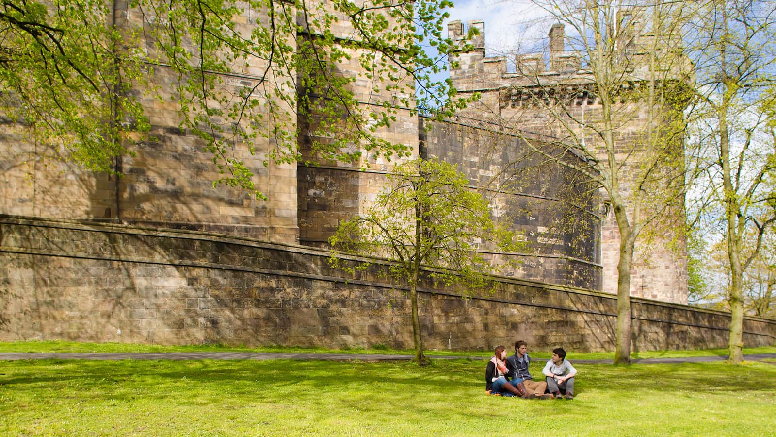Students sit on the grass outside the walls of Lancaster Castle
