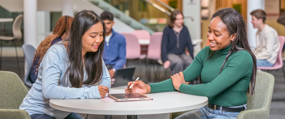 Two students sit at a desk in a modern atrium space.