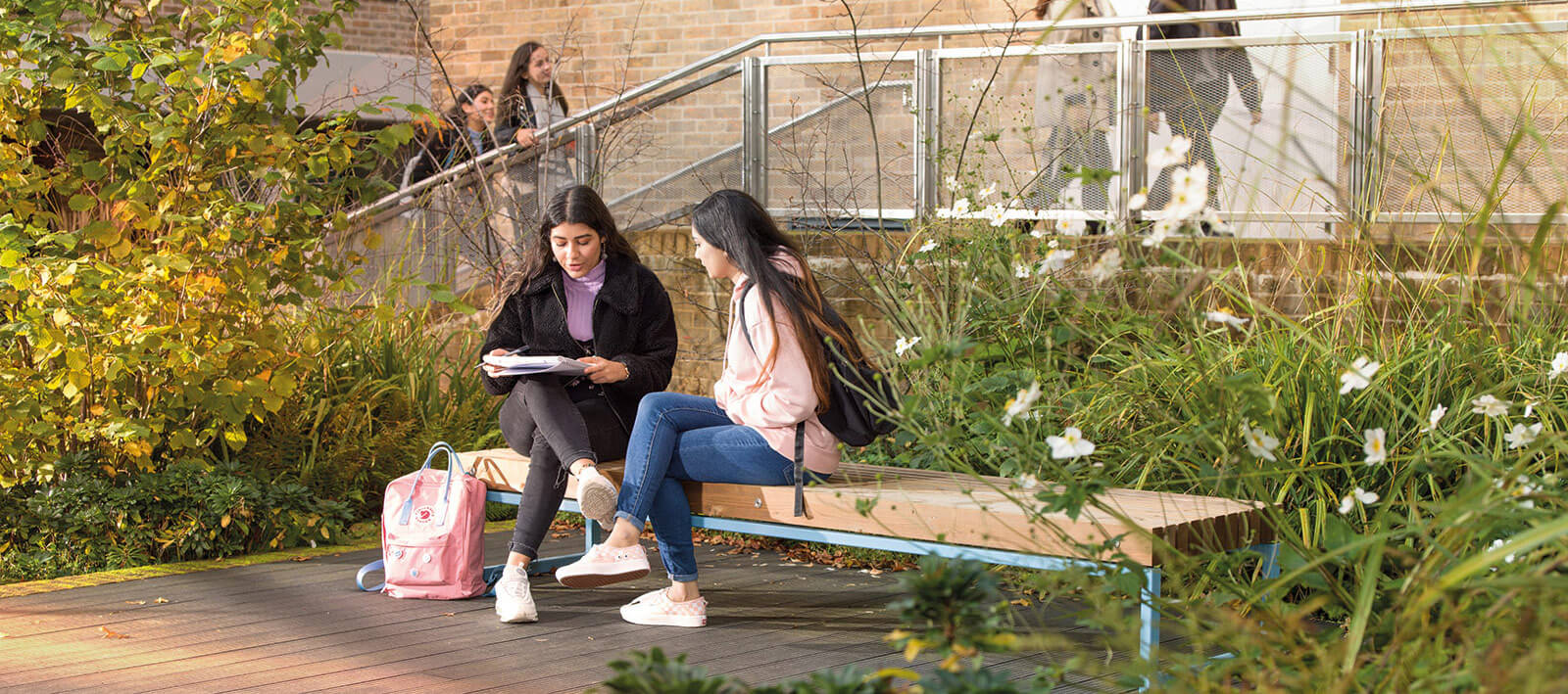 Tow female students sitting on a bench chatting and looking at a notepad