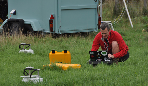 Researcher using scientific equipment in a grassland field.