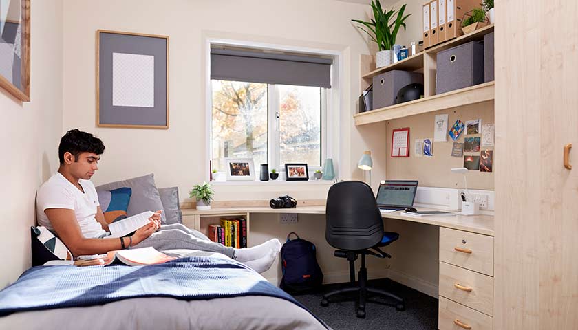 Student sitting on a bed in student accommodation on Lancaster University campus.