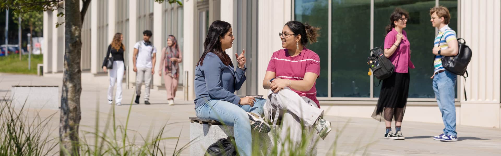 Students sat outside Lancaster University Management School smiling in the sun